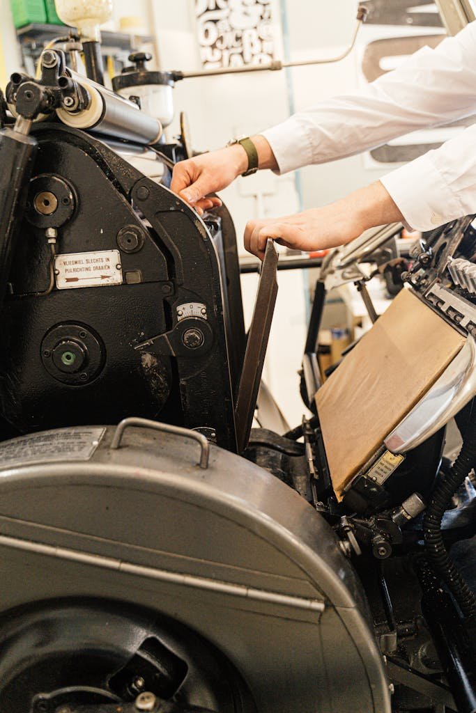 Close-up of hands adjusting a vintage printing press. Industrial machinery in use.